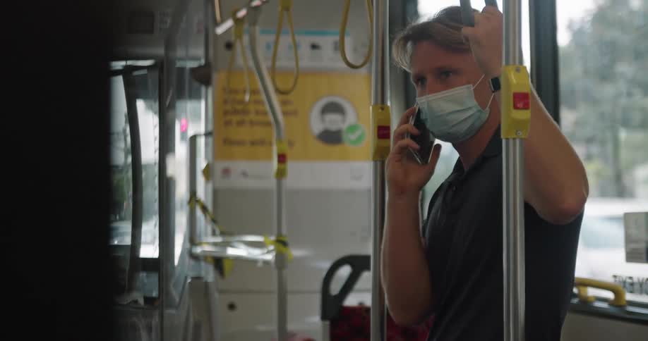 A man stands on a bus and talks on his cell phone