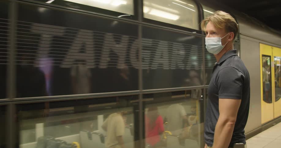 A man stands in a terminal watching the subway slow down in front of him