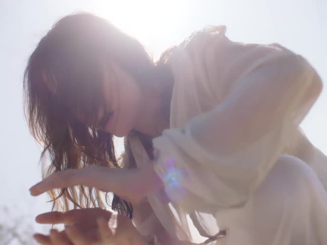 A woman in a white dress with trees the sun the sky and clouds in the background