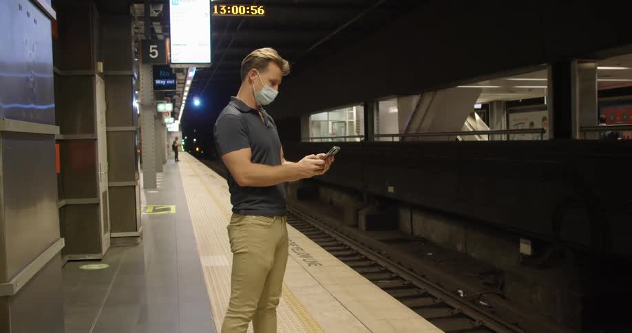 A man stands on a train platform and uses his cell phone
