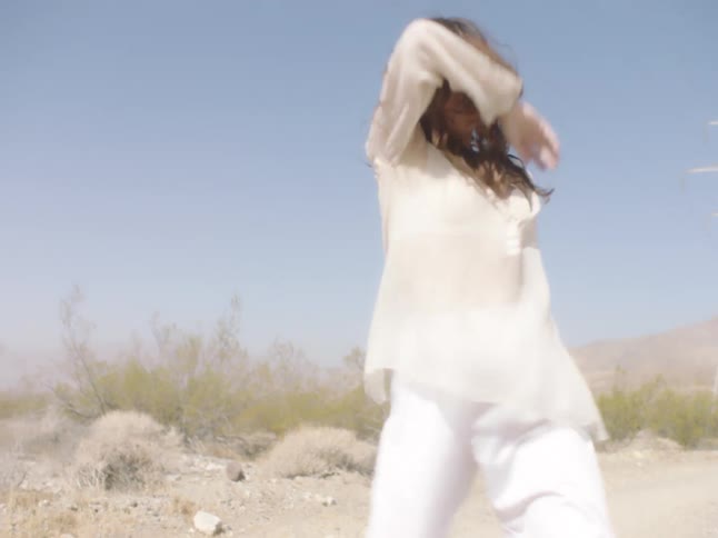 Young woman wearing white clothes dancing on a dirt road in the desert