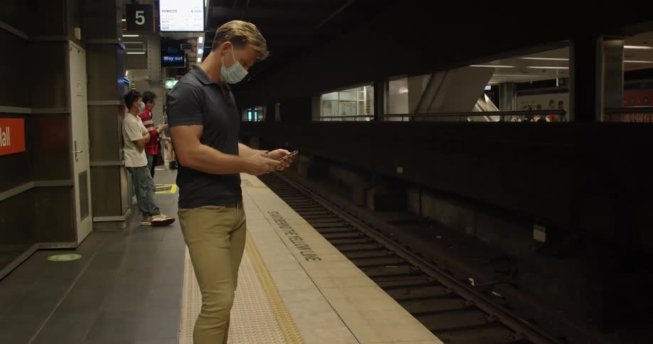 A man looks at his phone as he waits for a train at station