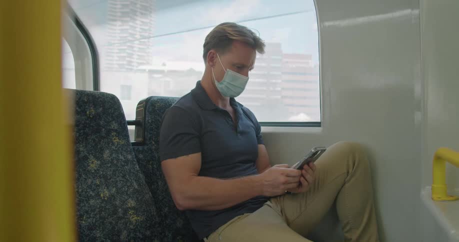 A man types on his smartphone while sitting on a train going through a city