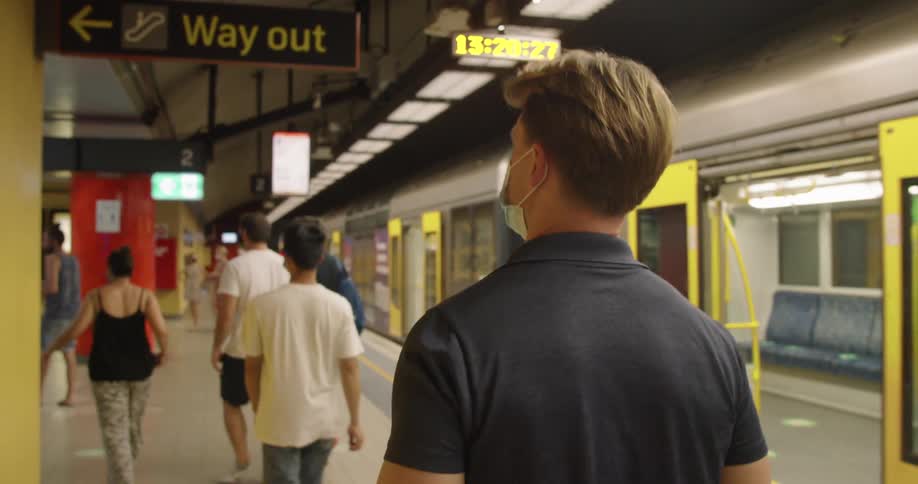 Man wearing a face mask walking on a train station at night