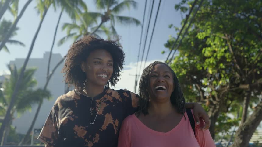 Two friends are laughing as they walk on a street side by side