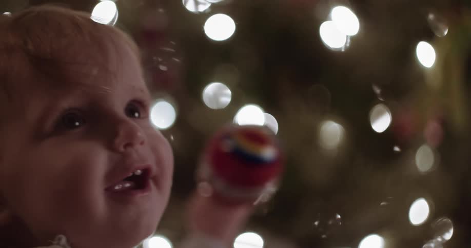 A baby is sitting in front of a christmas tree