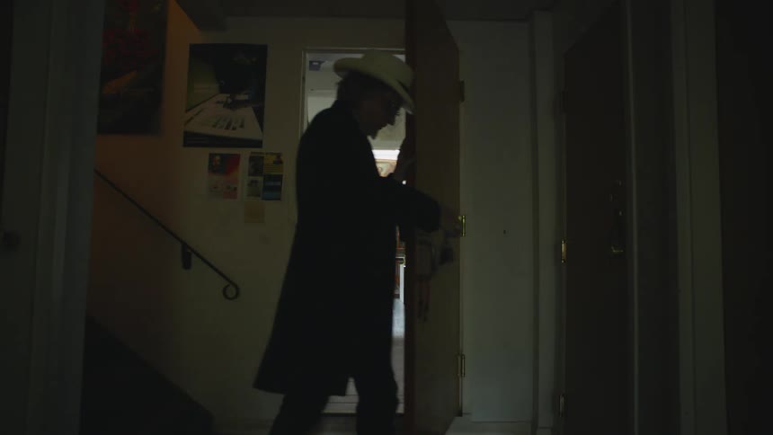 A man in a cowboy hat opens a door to his brightly lit classroom