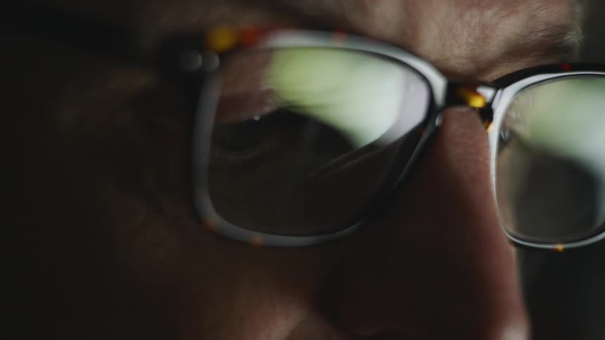 A man with glasses in a room staring off into the distance