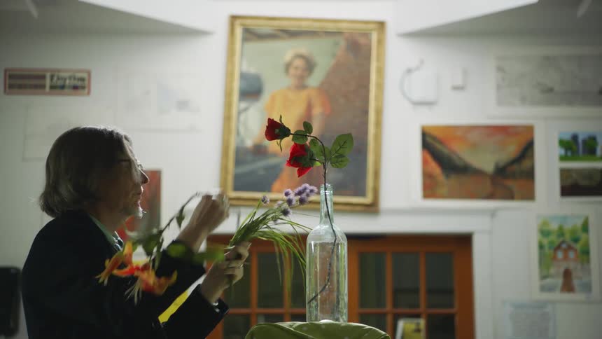 A man arranges wildflowers in a vase in an art classroom