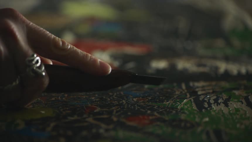 A person in a room with rings on their fingers using a tool to carve into a piece of wood