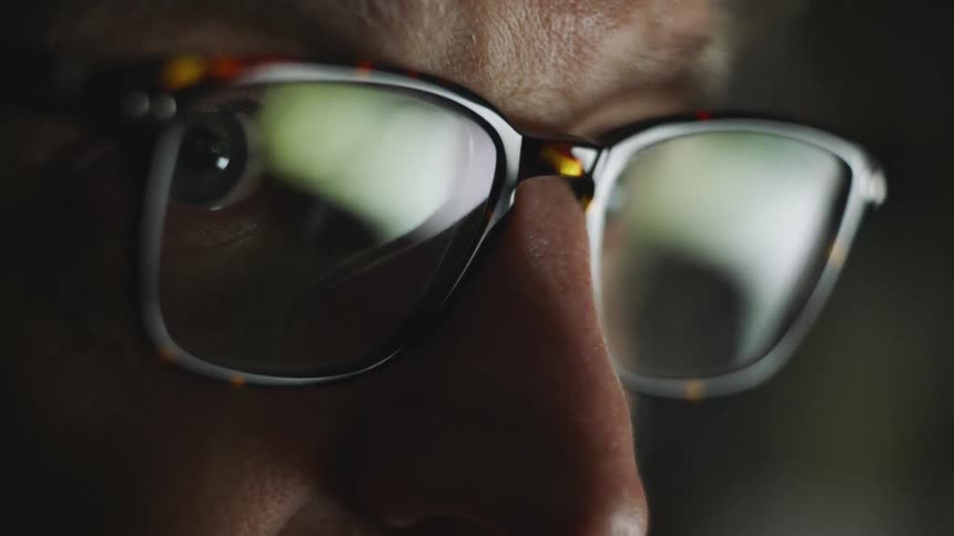 A man with glasses in a room staring off into the distance