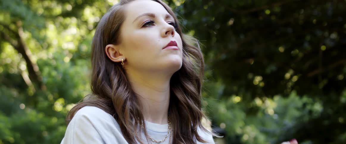 A woman with makeup outside with trees and leaves in the background