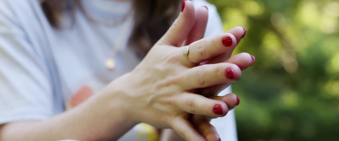 A woman with rings on her finger with trees and leaves in the background