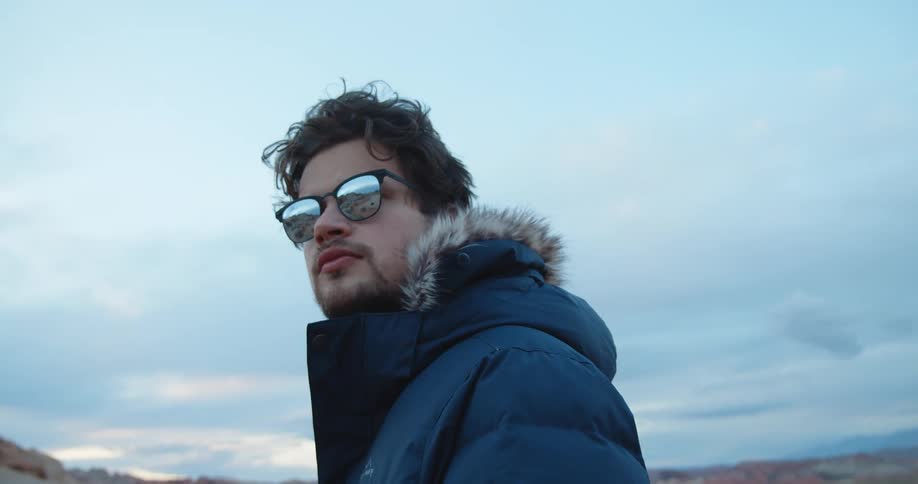 A man stands and looks around while standing in a desert in a winter parka