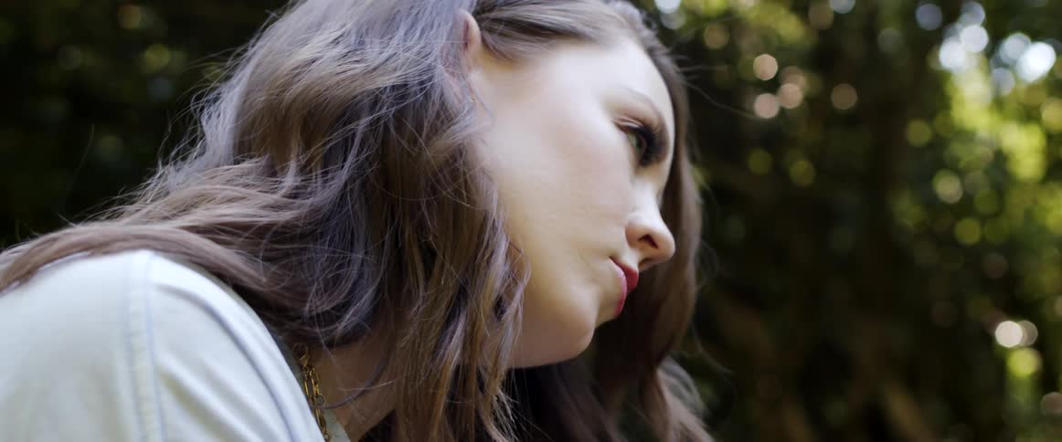 A young woman raises her head contemplatively while sitting outdoors during the day