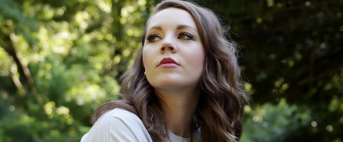 A young woman gazes around at her surroundings while sitting outdoors on a sunny day