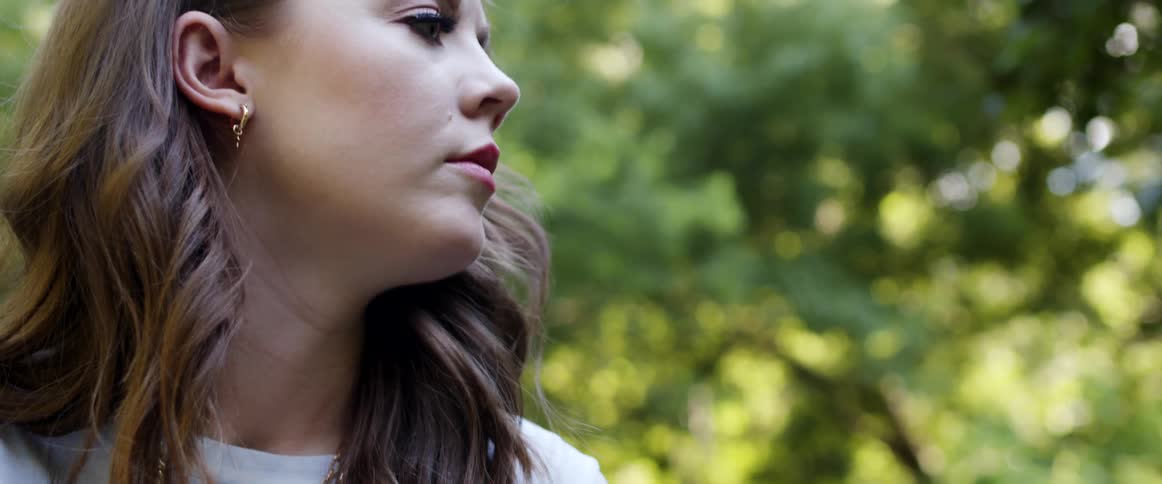 A woman sitting on the grass rubs her hands together as she thinks
