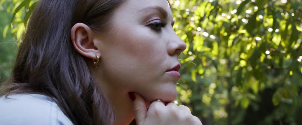 A woman rests her face on her hands as she sits and looks at the trees on a sunny day