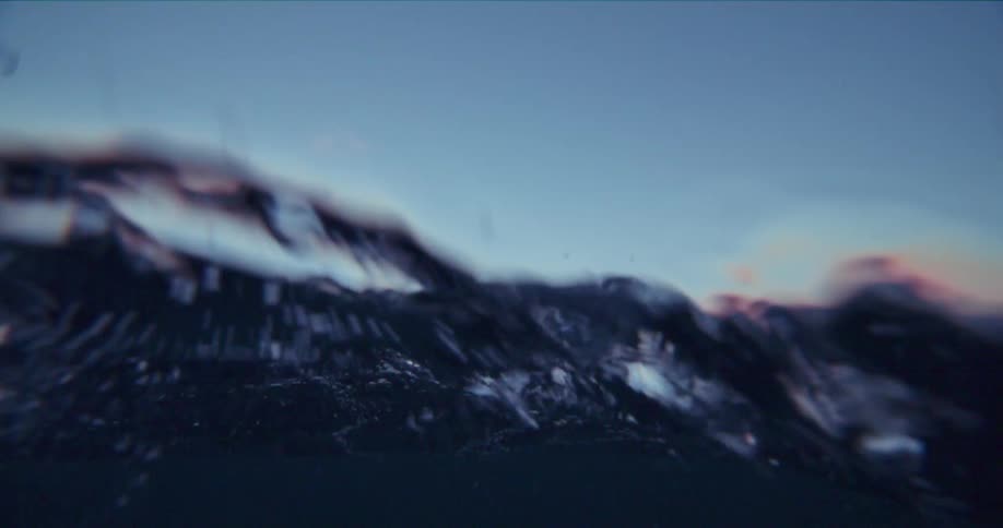 Rolling waves with seagulls flying above the surface near jagged rocky land at sunset