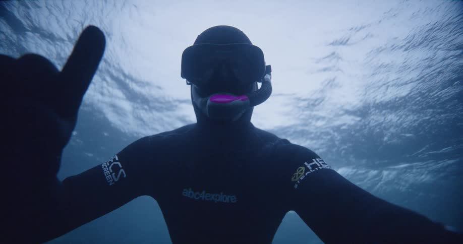 A person with goggles a snorkel and a wetsuit swimming underwater with the sky and clouds above