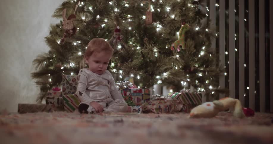 A child sits near presents under a christmas tree