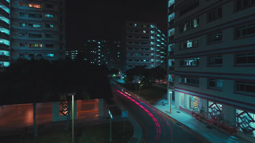 Lights of vehicle leave streak as vehicle moves around corner past buildings at night