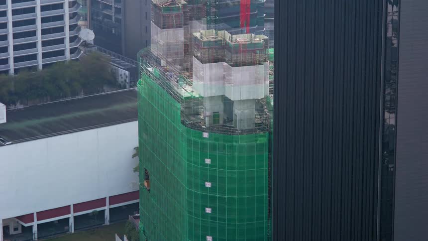 A building being constructed with a construction crane and people with trees in the background