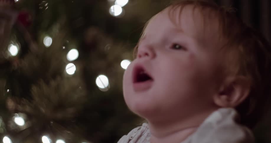 A toddler sits in front of a lit christmas tree