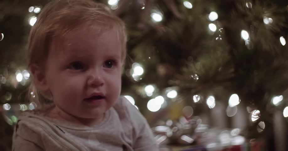 A toddler sits in front of a lit christmas tree