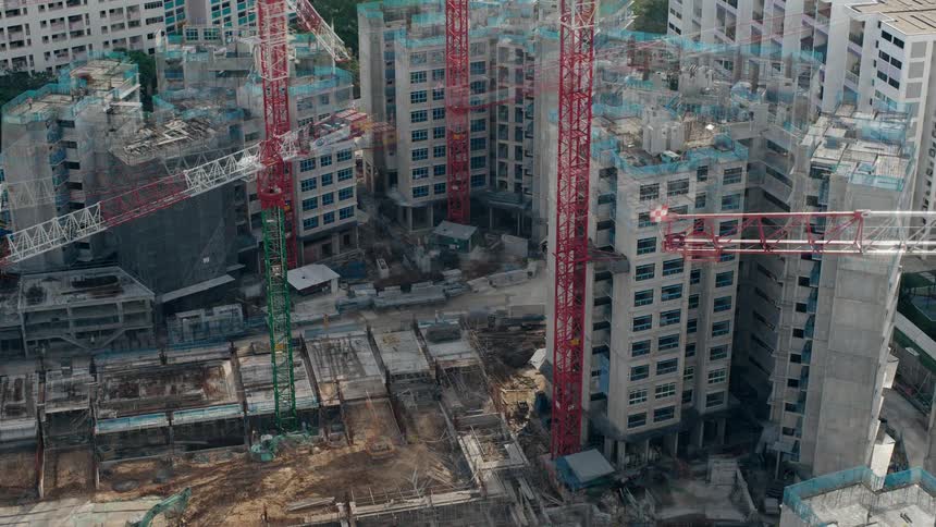 Workers and cranes move along building construction site near other buildings