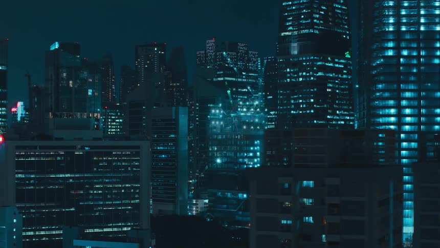 Lights on city buildings and construction cranes flash and glow at night