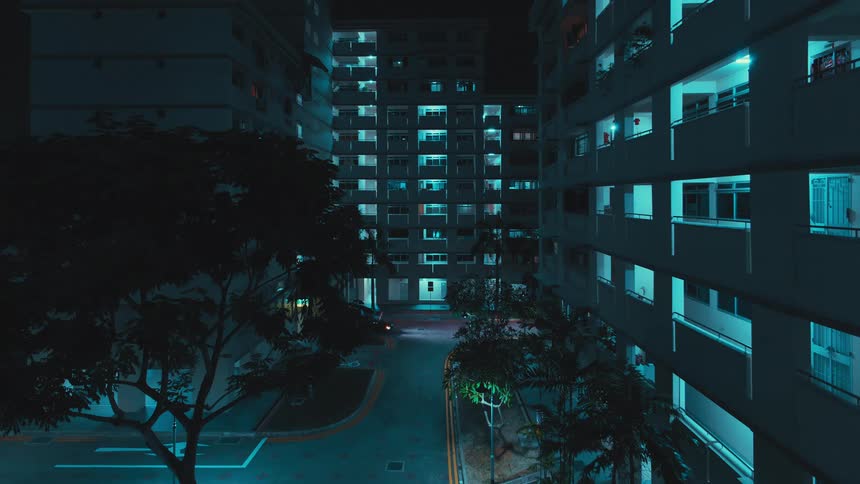 A vehicle travels along a road between buildings in a metropolis at night