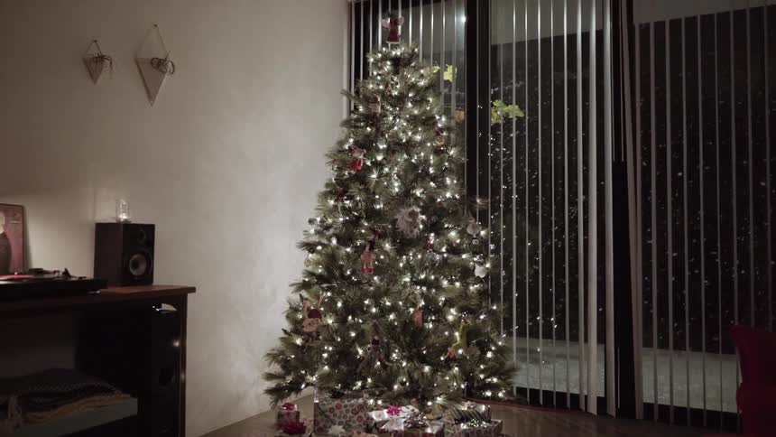View of a brightly lit christmas tree as it snows outside