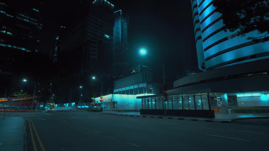Vehicle lights leave streaks as traffic flows along street between buildings at night