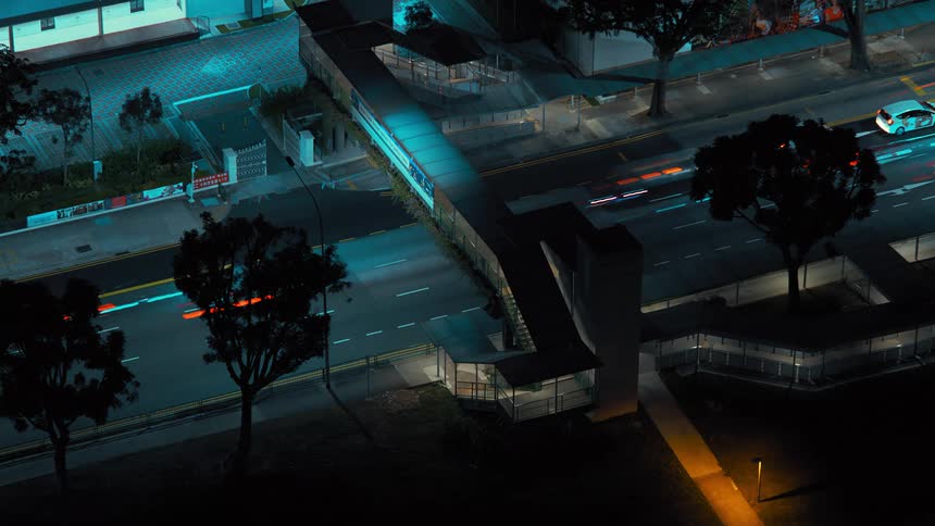 Cars travel under a pedestrian walkway on a city street at night