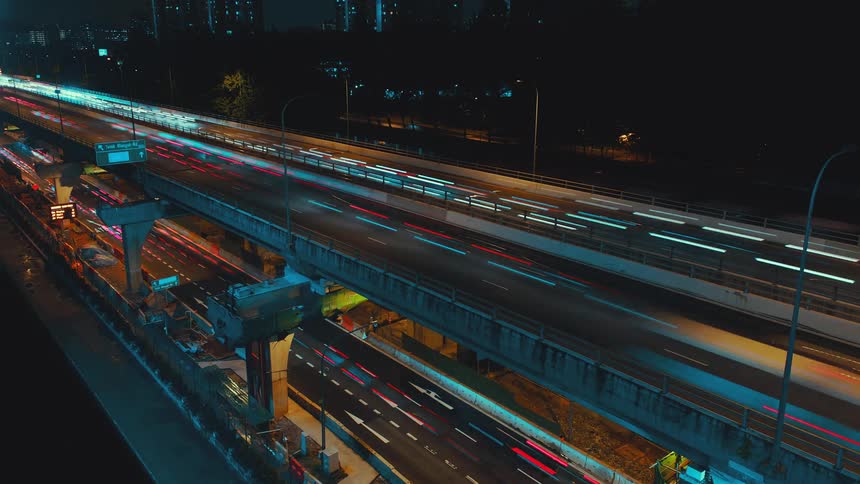 A highway with streetlights and vehicles with trees and buildings in the background