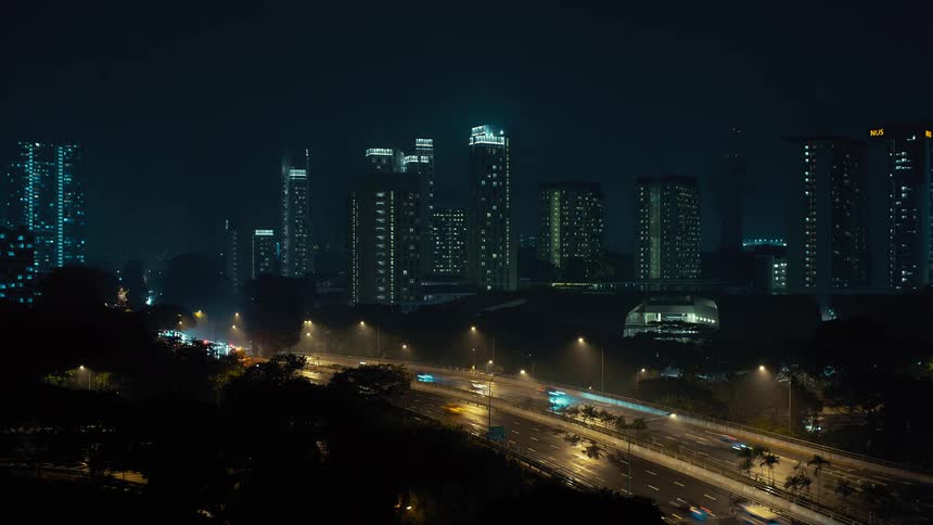 Vehicles drive past a building as its lights turn on