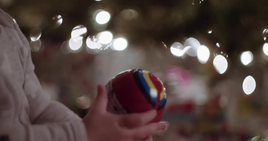 Young child holding a colorful round object in front of a christmas tree