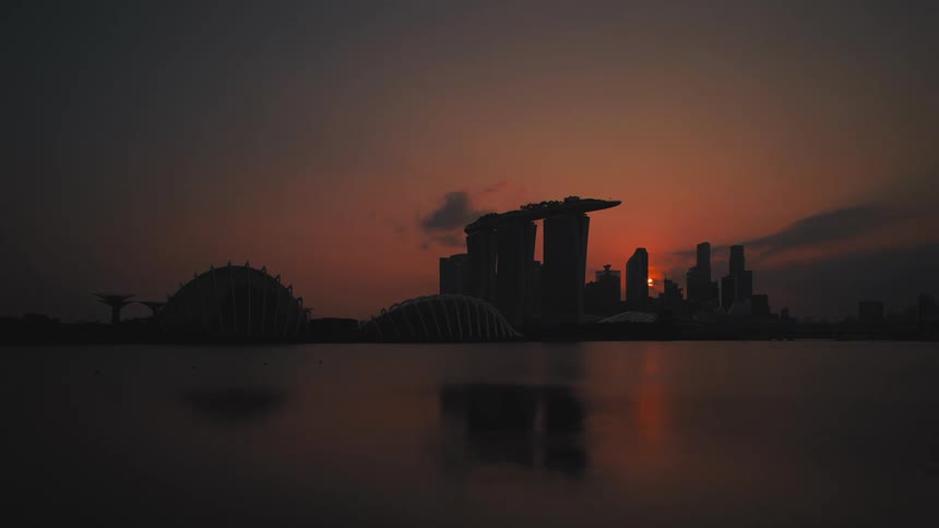A coastal city skyline is illuminated and then silhouetted by the setting sun