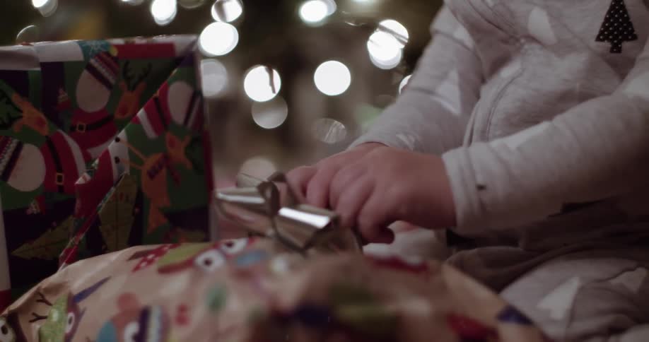 Young child admiring a silver bow on a present with a christmas tree in the background