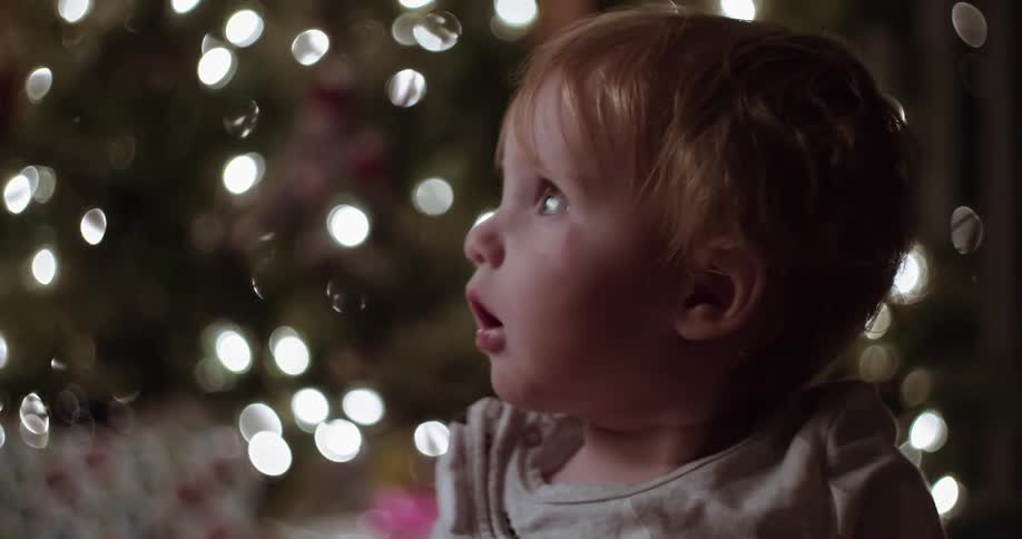 Infant sitting in front of a christmas tree and looking around