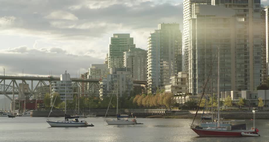 Boats float in Vancouver's False Creek harbor with glass condos lining the seawall at sunset
