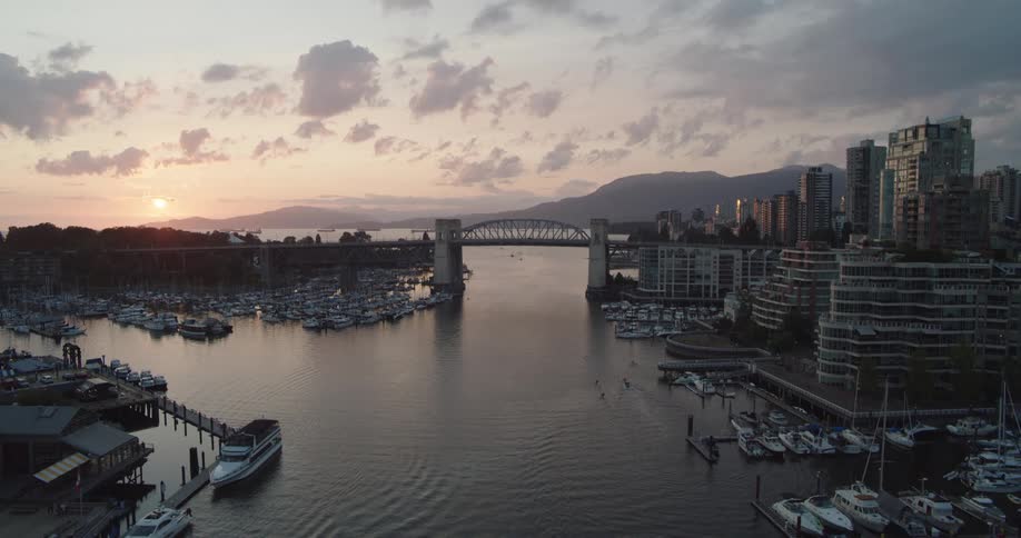 The sun sets behind Burrard Bridge in Vancouver as boats exit the waterway by the seawall