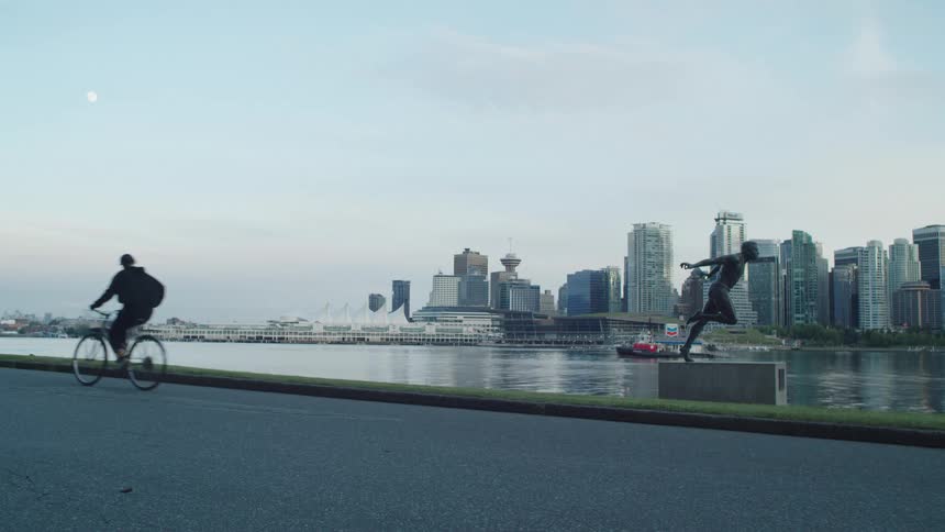 A person rides a bicycle past the Harry Jerome statue in Stanley Park with the Vancouver city skyline behind