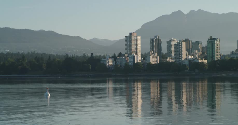 The Ocean with a city skyline featuring buildings and a mountain range in the background at sunrise