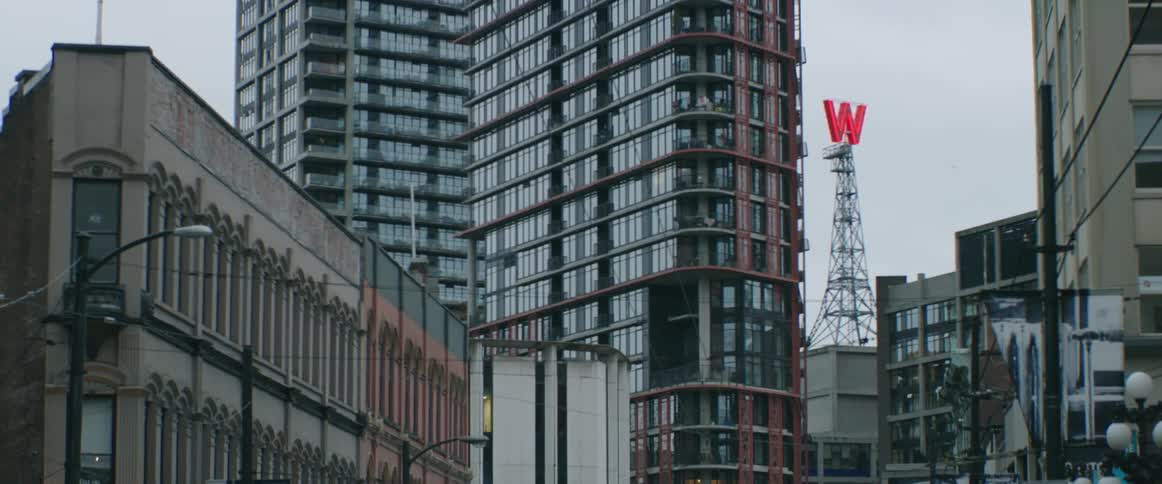 A red letter w rotates on a tower behind city buildings on a cloudy day