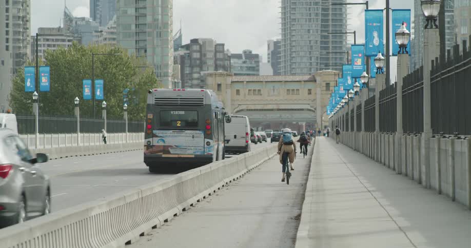 People on sidewalks and bicycles and in vehicles and buses all head on city streets toward downtown