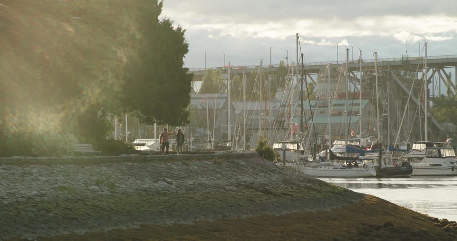 A man and woman walk on a seawall past a marina full of boats
