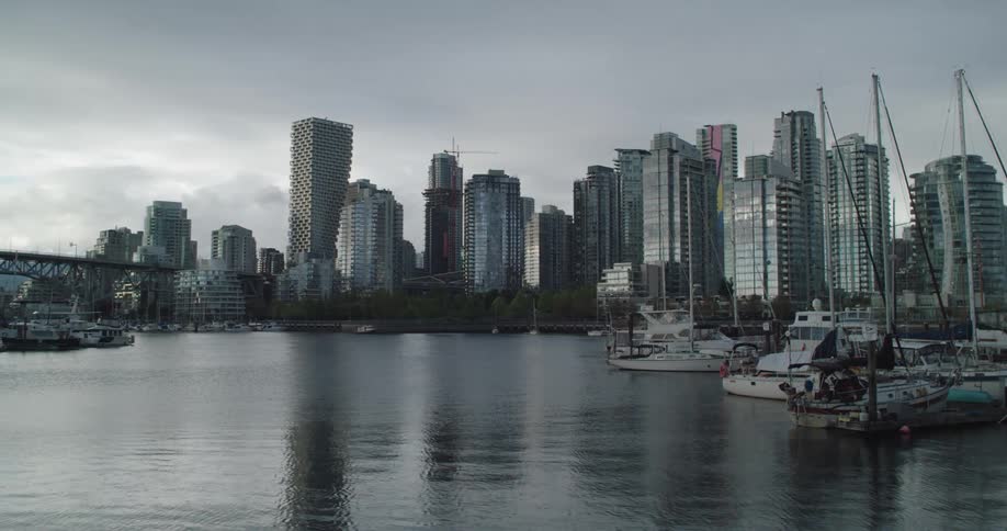 Rippling water reflects boats at marina and city skyscrapers under overcast sky