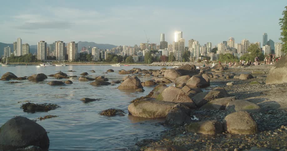Water laps gently against the rocks and shore with a city skyline behind